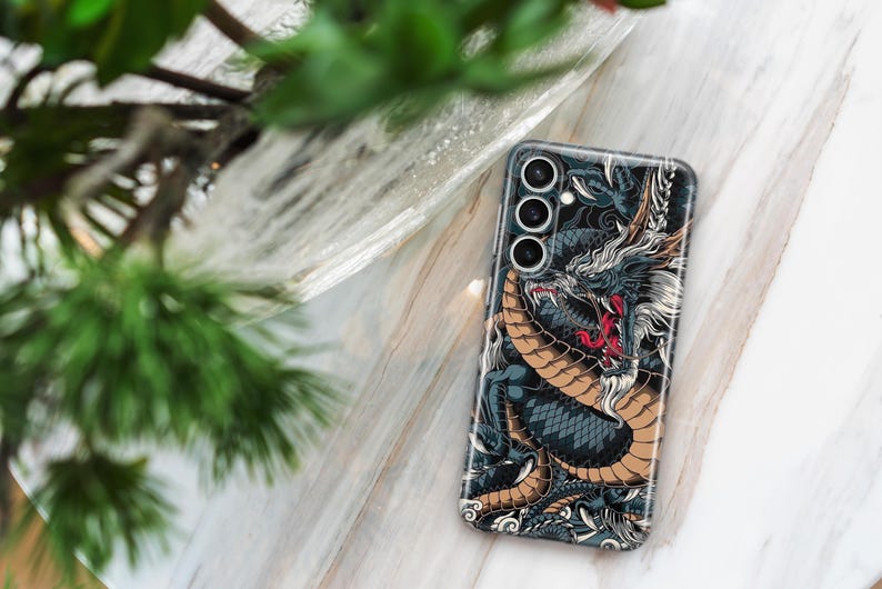 Pu&ograve; includere: Una custodia per telefono nera con un'illustrazione dettagliata di un drago con accenti dorati e rossi. La custodia per telefono ha un ritaglio per l'obiettivo della fotocamera con tre cerchi.