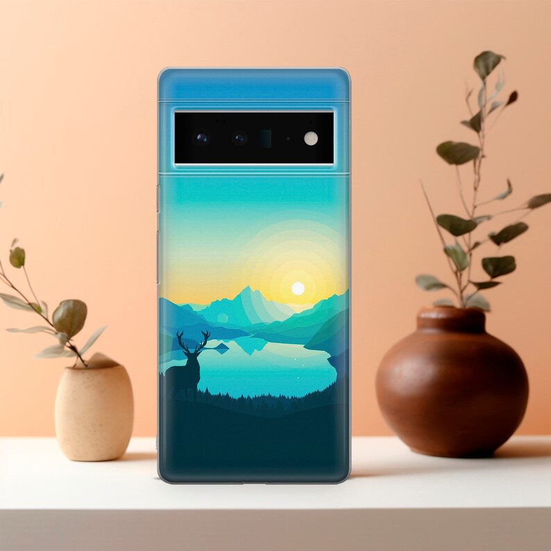 May include: A clear phone case featuring a scenic landscape design. The image depicts a mountain range, a lake, a deer, and a sunset. The case is designed for a phone with a triple camera system.