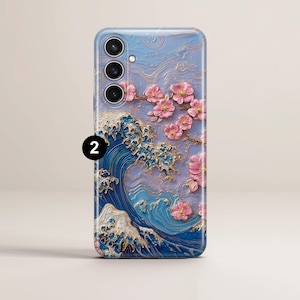 May include: A phone case featuring a 3D design of a Japanese wave with gold accents and pink cherry blossoms. The case has a blue and purple background with a textured appearance, and a camera cutout.