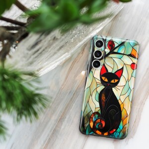 May include: A black cat with yellow eyes sits in a stained glass design on a phone case. The case has a multi-colored background with a floral design. The phone case has a camera lens cutout with three lenses.