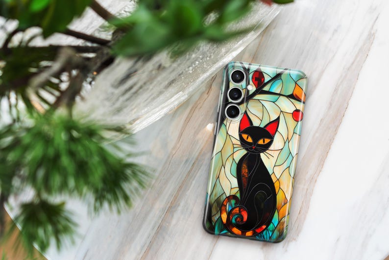 May include: A black cat with yellow eyes sits in a stained glass design on a phone case. The case has a multi-colored background with a floral design. The phone case has a camera lens cutout with three lenses.