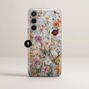 May include: A phone case with a floral design. The case features a variety of flowers in shades of pink, orange, and white, set against a light background. The case has a camera module with three lenses.
