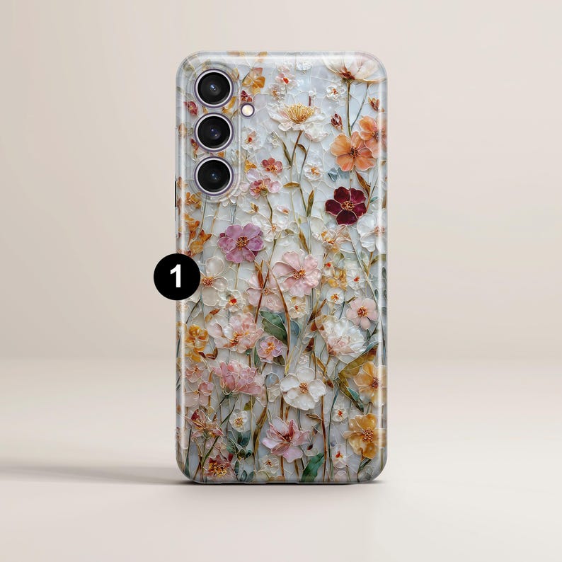 May include: A phone case with a floral design. The case features a variety of flowers in shades of pink, orange, and white, set against a light background. The case has a camera module with three lenses.