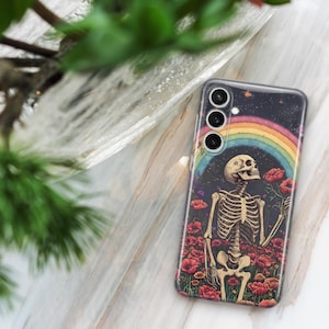 May include: A phone case featuring a colourful rainbow and a skeleton holding a flower. The background is a dark blue with stars. The phone case has a multi-lens camera.