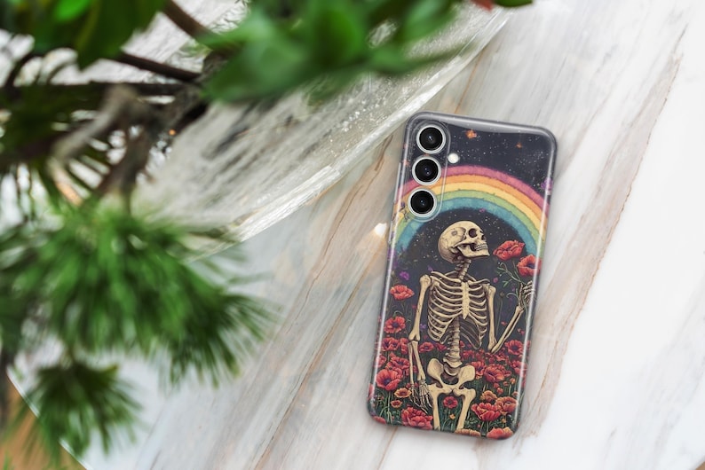 May include: A phone case featuring a colourful rainbow and a skeleton holding a flower. The background is a dark blue with stars. The phone case has a multi-lens camera.