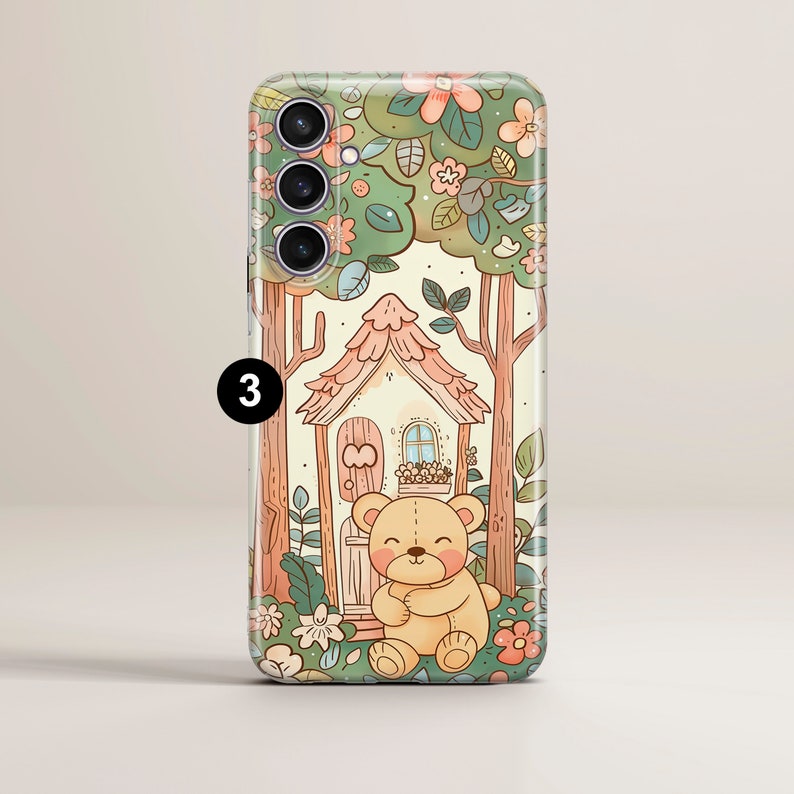 May include: A phone case with a cute cartoon illustration of a teddy bear sitting in front of a small house in a forest. The house has a pink roof and a brown door. The forest is filled with green trees and pink flowers.