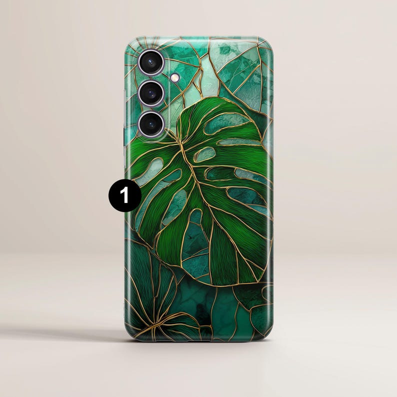 May include: A phone case featuring a green and gold leaf design. The case has a glossy finish and a detailed illustration of a monstera leaf with gold outlines. The background has a mosaic-like pattern in shades of green.