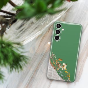 May include: A green smartphone case with a floral design. The case features a collage of dried flowers, butterflies, and newsprint. The phone case is resting on a marble surface, with green foliage in the background.