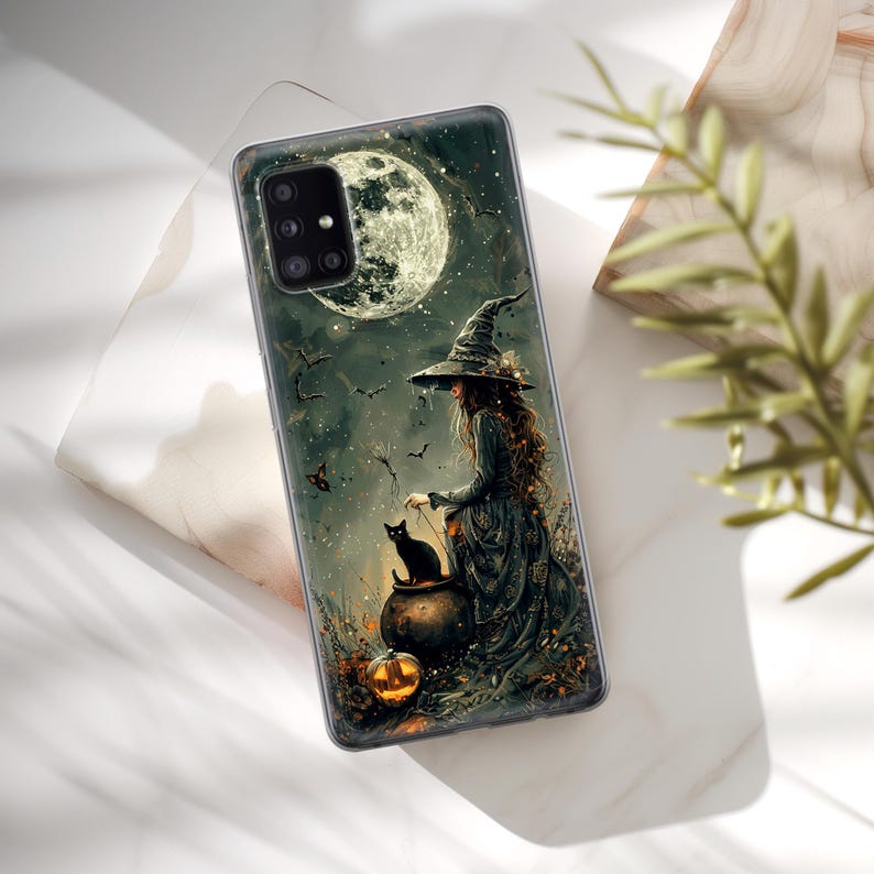 May include: A phone case with a witch and a black cat in front of a full moon. The witch is wearing a black hat and dress. The cat is sitting on a cauldron. There is a pumpkin in the foreground.