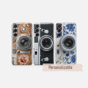 May include: Three rectangular phone cases featuring camera-themed designs. The left case has a tan floral pattern with a rose. The center case is black with a textured leather look. The right case has a blue and white floral pattern. Text reads Personalizable.