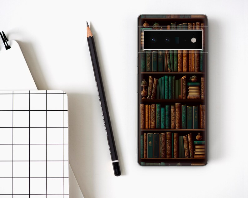 May include: A smartphone case featuring a detailed illustration of a bookshelf filled with books in shades of brown and green. A black pencil and a white notebook with a grid pattern are also visible.