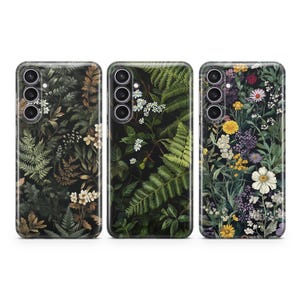 May include: Three phone cases with different floral designs. The first case features a dark green and brown fern pattern. The second case has a dark green fern and white flower pattern. The third case has a colourful floral pattern with yellow, white, and purple flowers.