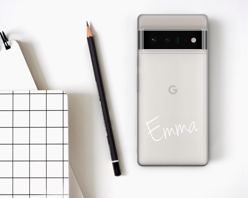 Op de afbeelding: Een witte telefoonhoes met een zwarte camera lens en de naam "Emma" in wit schrift op de achterkant.