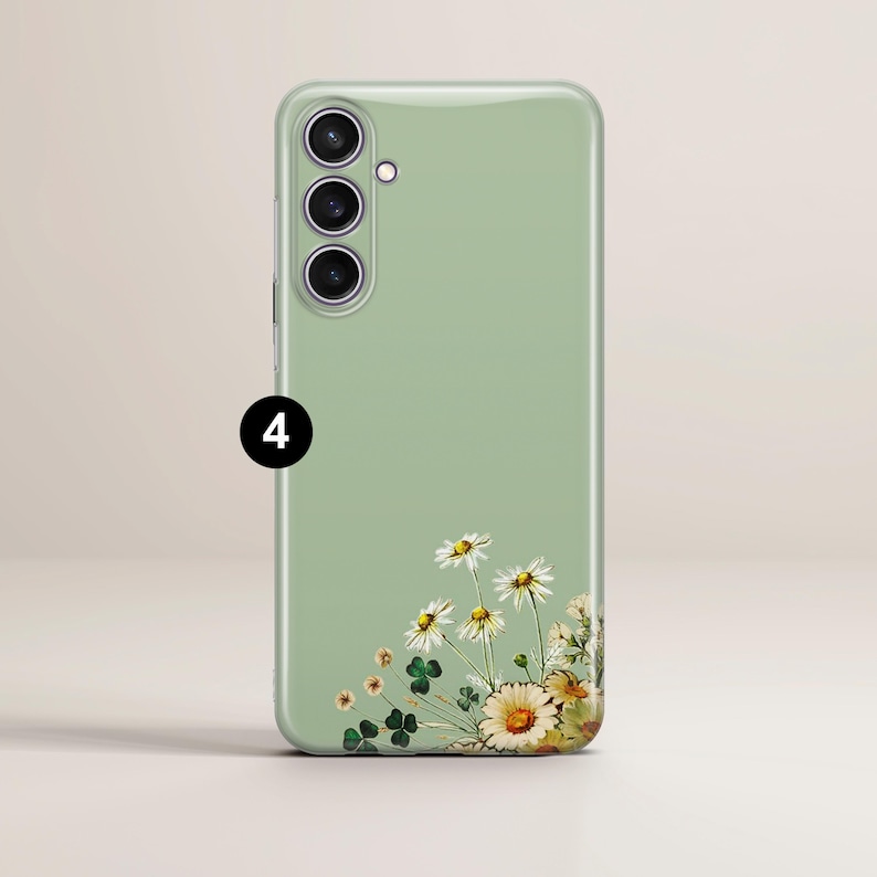 May include: A light green phone case featuring a floral design of white daisies and yellow-centered flowers. The case has a smooth finish and a camera module with three lenses. The floral arrangement is in the lower right corner.