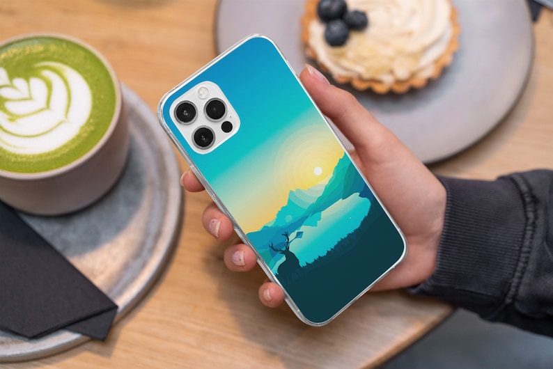 May include: A clear phone case with a colorful landscape design. The case features a blue sky, green mountains, and a lake with a deer silhouette. The case is designed for a phone with a triple camera system.