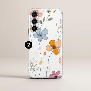May include: A white phone case featuring a floral design with pastel-colored flowers and green leaves. The flowers are in shades of orange, blue, pink, and peach, with black line art. The phone case has a camera module with three lenses.