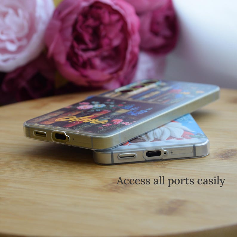 May include: Two phone cases stacked on a wooden surface. The top case has a floral design with the word "Aura" in gold lettering. The bottom case has a white flower design. The text "Access all ports easily" is visible.