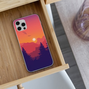 May include: A phone case with a sunset landscape design. The case features a silhouette of mountains, trees, and a bright orange sun. The case is made of a durable material and is designed to protect your phone from scratches and bumps.