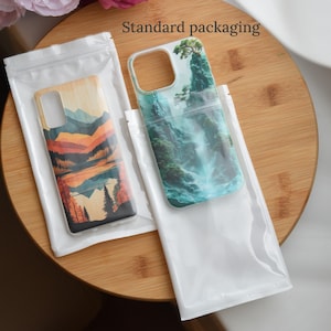 May include: Two phone cases in clear plastic packaging. One case has a wooden finish with a mountain and lake design in orange, red, and brown. The other case features a waterfall scene with green and blue hues. The text "Standard packaging" is visible.