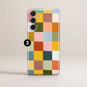 May include: A smartphone case with a colorful, abstract checkerboard pattern. The design features squares of various colors, including pink, yellow, green, and brown. The case has a camera module with three lenses and a flash.