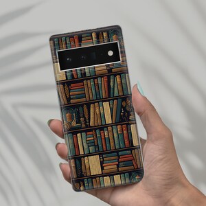 May include: A smartphone case featuring a detailed illustration of a bookshelf filled with various books. The design incorporates a dark background with rows of books in shades of blue, brown, and gold. The case is held in a person's hand.