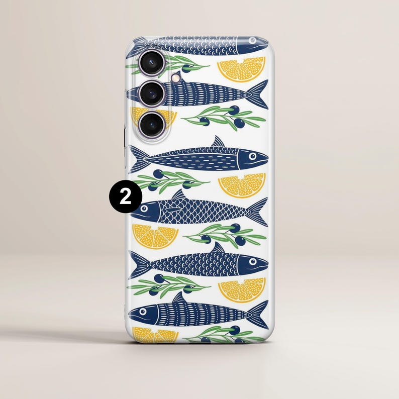 May include: A white phone case with a repeating pattern of navy blue fish, yellow lemon slices, and olive branches. The design has a nautical theme. The phone case has a camera cutout with three lenses.