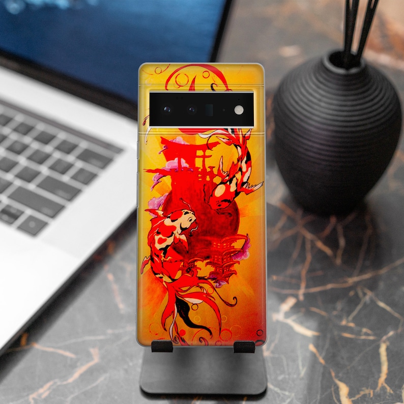 May include: A yellow, red, and black phone case with a Japanese-inspired design featuring two koi fish swimming around a red temple. The case has a black camera cutout and a black stand.