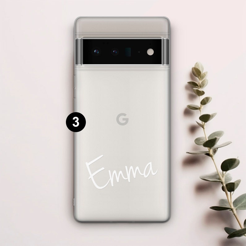 Op de afbeelding: Een witte telefoonhoes met een transparante achterkant en een zwarte camera lens. De hoes heeft een wit Google logo en de naam "Emma" in wit cursief.