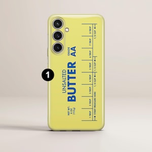 May include: A yellow phone case with a blue and white design that says "Unsalted Butter AA" and has a measurement guide for tablespoons and cups. The case is for a phone with a triple camera lens.
