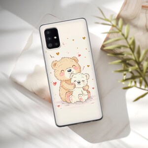 May include: A white phone case with a cute illustration of two teddy bears hugging. The larger bear is brown and the smaller bear is white. The background is white with pink and gold hearts.