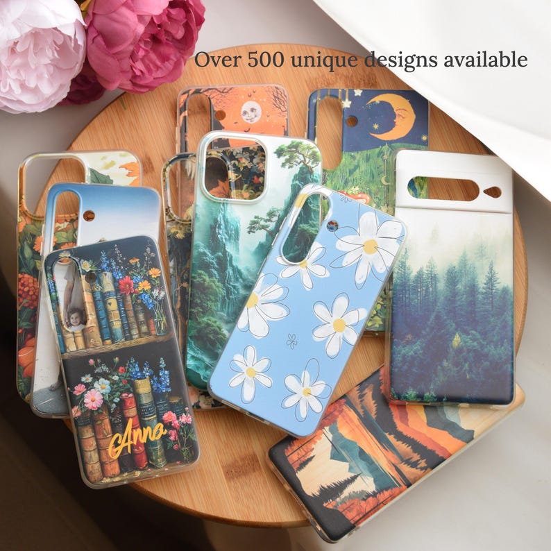 May include: A collection of phone cases with various designs, including floral, landscape, and celestial themes. One case features white daisies on a light blue background. The text "Over 500 unique designs available" is visible.