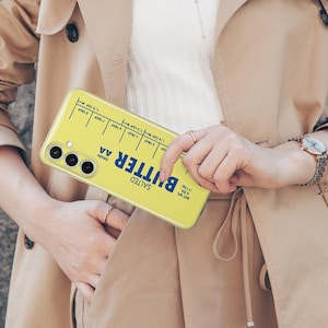 May include: A yellow phone case with a design that looks like a stick of butter. The case has the words "Salted Butter AA Grade" printed on it, along with a measurement guide for tablespoons and cups.