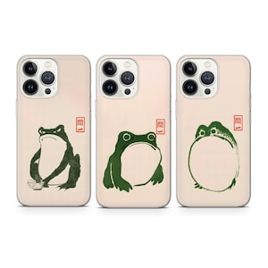 Puede incluir: Tres fundas para teléfono con diferentes ilustraciones de ranas. Las fundas son transparentes y tienen un fondo blanco. Las ranas son verdes y tienen diferentes poses. El texto en las fundas dice "関".