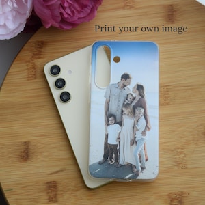 May include: A smartphone case with a family photo print. The case is clear with a blue and white sky design at the top. The phone is a light beige color. The text "Print your own image" is visible.