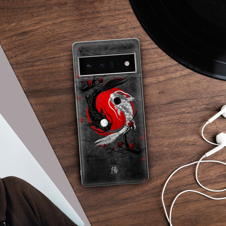 May include: A black phone case with a yin yang design featuring two koi fish swimming around a red circle. The case has a textured, gray background and the word "陰陽" in white text.