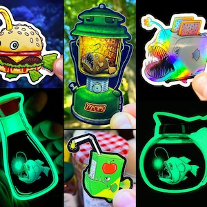 May include: Set of six glow-in-the-dark stickers featuring a deep sea anglerfish in various settings. The stickers include a burger, a lantern, a toaster, a coffee pot, a juice box, and a bottle of soy sauce.