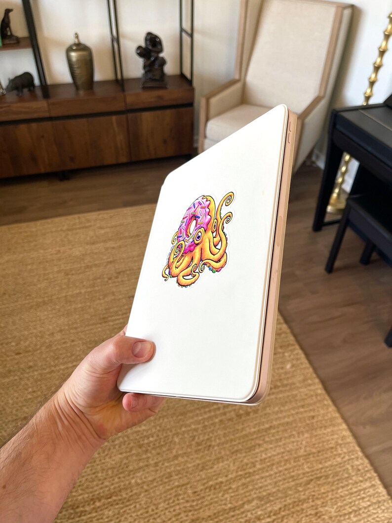 May include: A white iPad case with a colorful illustration of an octopus holding a donut. The donut is pink with white sprinkles and the octopus is yellow with purple tentacles.