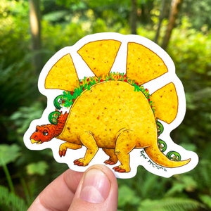 May include: A yellow and brown cartoon dinosaur with a taco shell for a back. The dinosaur has green lettuce, red tomatoes, and white sour cream inside the taco shell. The dinosaur is standing on a white background. The artist's signature, "Ryan McCulloch", is written on the dinosaur's tail.