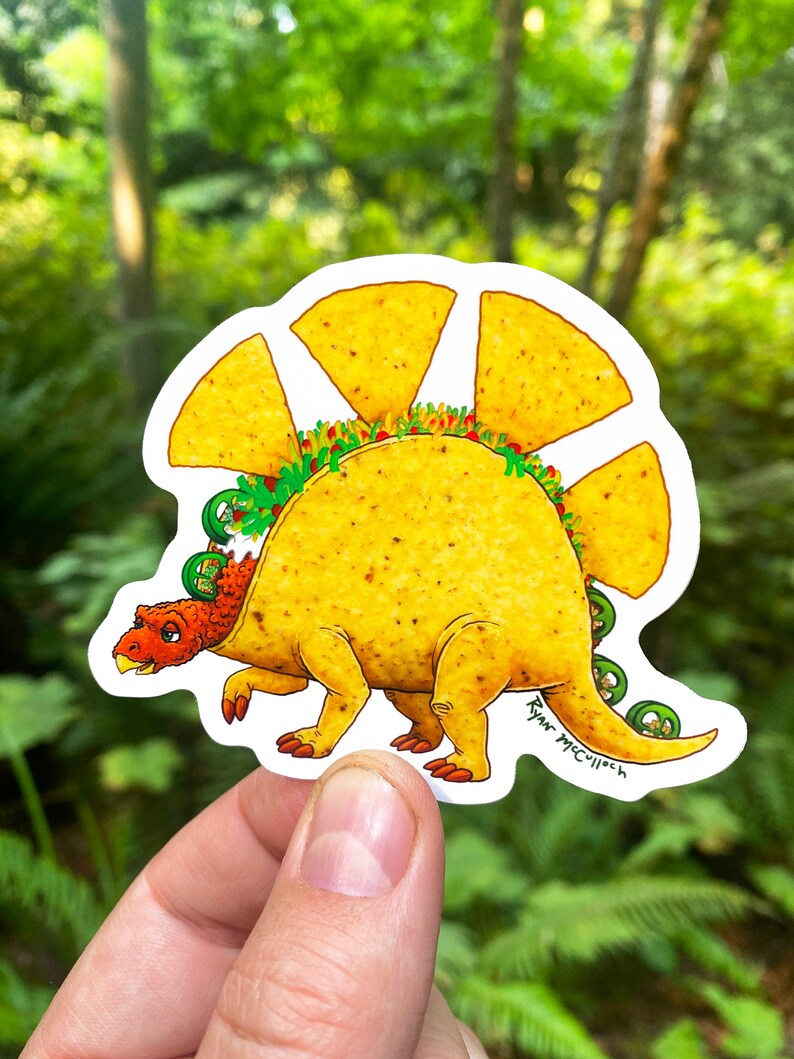 May include: A yellow and brown cartoon dinosaur with a taco shell for a back. The dinosaur has green lettuce, red tomatoes, and white sour cream inside the taco shell. The dinosaur is standing on a white background. The artist's signature, "Ryan McCulloch", is written on the dinosaur's tail.