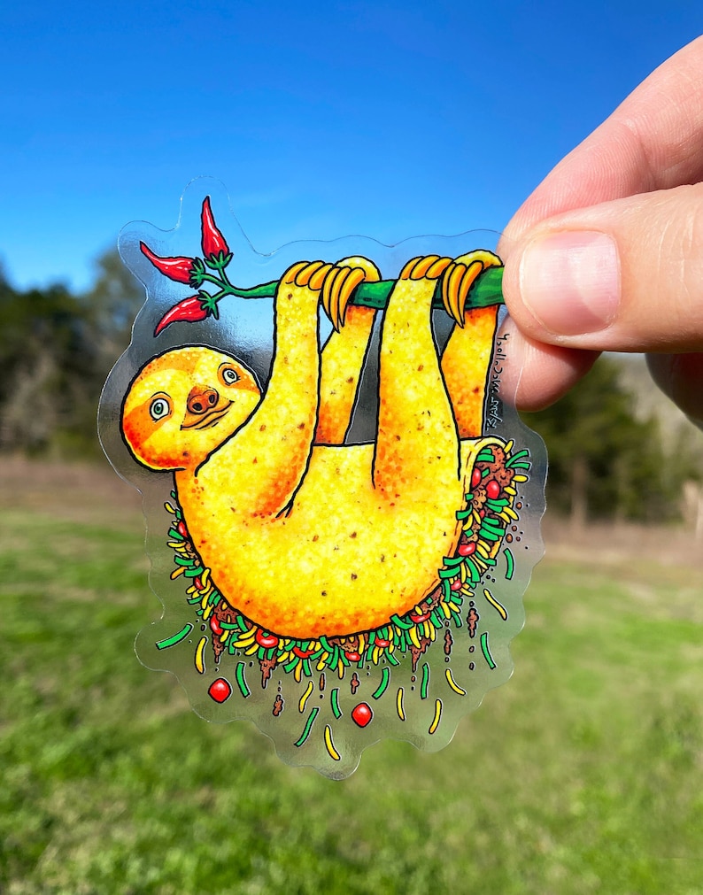May include: A yellow sloth hanging upside down with a green branch and red peppers. The sloth is surrounded by a green, yellow, and brown border that looks like a taco.
