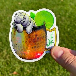 May include: A sticker featuring a manatee relaxing in a copper mug. The mug is adorned with a lime slice and mint sprig. The sticker has the text "Ryan McCulloch" on the handle.