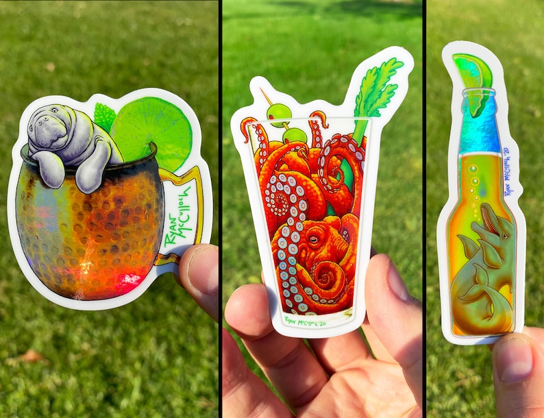 May include: Set of three stickers featuring whimsical illustrations. One shows a manatee in a copper mug with a lime, another depicts an octopus in a cocktail glass, and the last one has dolphins in a beer bottle with a lime wedge.