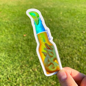 May include: A sticker in the shape of a beer bottle with a lime wedge on top. Inside the bottle are two dolphins. The bottle has a gradient of colors, including blue, yellow, and green. The text "Ryan Mcclintock 20" is on the bottle.