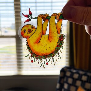 May include: A yellow sloth hanging upside down from a branch with red peppers. The sloth is filled with a colorful taco filling, including lettuce, tomatoes, cheese, and meat. The text "Ryan MCCLURE" is written on the sticker.