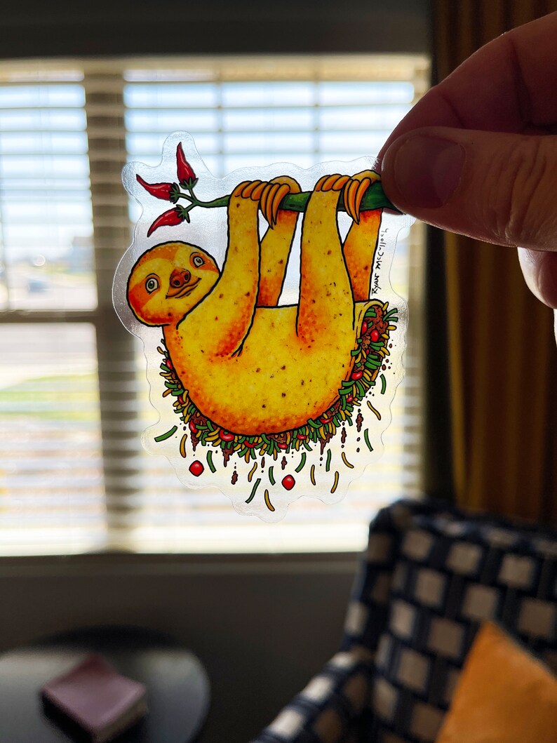 May include: A yellow sloth hanging upside down from a branch with red peppers. The sloth is filled with a colorful taco filling, including lettuce, tomatoes, cheese, and meat. The text "Ryan MCCLURE" is written on the sticker.