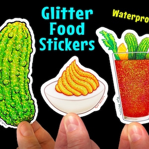 May include: Three glitter food stickers featuring a green pickle, a deviled egg with yellow yolk, and a red bloody mary with green celery stalks and olives. The stickers are waterproof and have the text "Glitter Food Stickers" and "Waterproof!" printed on them.
