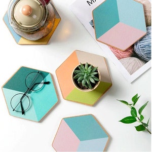May include: Geometric coasters in teal, pink, orange, and green with a natural cork edge. One coaster holds a small succulent plant in a beige pot. A pair of round-framed glasses rests on a teal and green coaster.