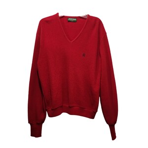 May include: A red v-neck sweater with long sleeves and a small embroidered logo on the chest. The sweater is made of a soft, textured fabric.