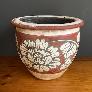 May include: A white ceramic mug with a black handle and the text "But First, Coffee" in a bold, black font. The mug is set against a blurred background, suggesting a cozy setting.