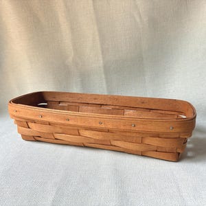 May include: A rectangular woven wood basket with a light brown finish. The basket features a flat base and vertical sides constructed from thin, interlaced wooden strips, secured with small metal nails along the top rim of the structure.